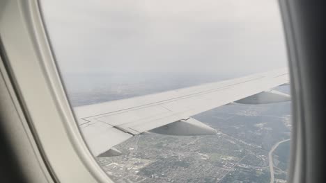 Vista-Desde-La-Ventana-De-Un-Avión-Volando-Sobre-Una-Ciudad-Durante-El-Día