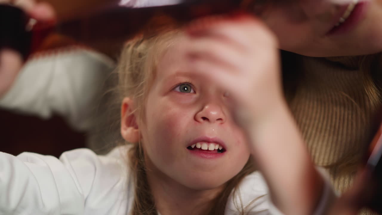 Girl looks at processed film with family shots near mother