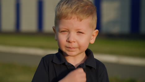 little boy touches nose and smiles standing on city street