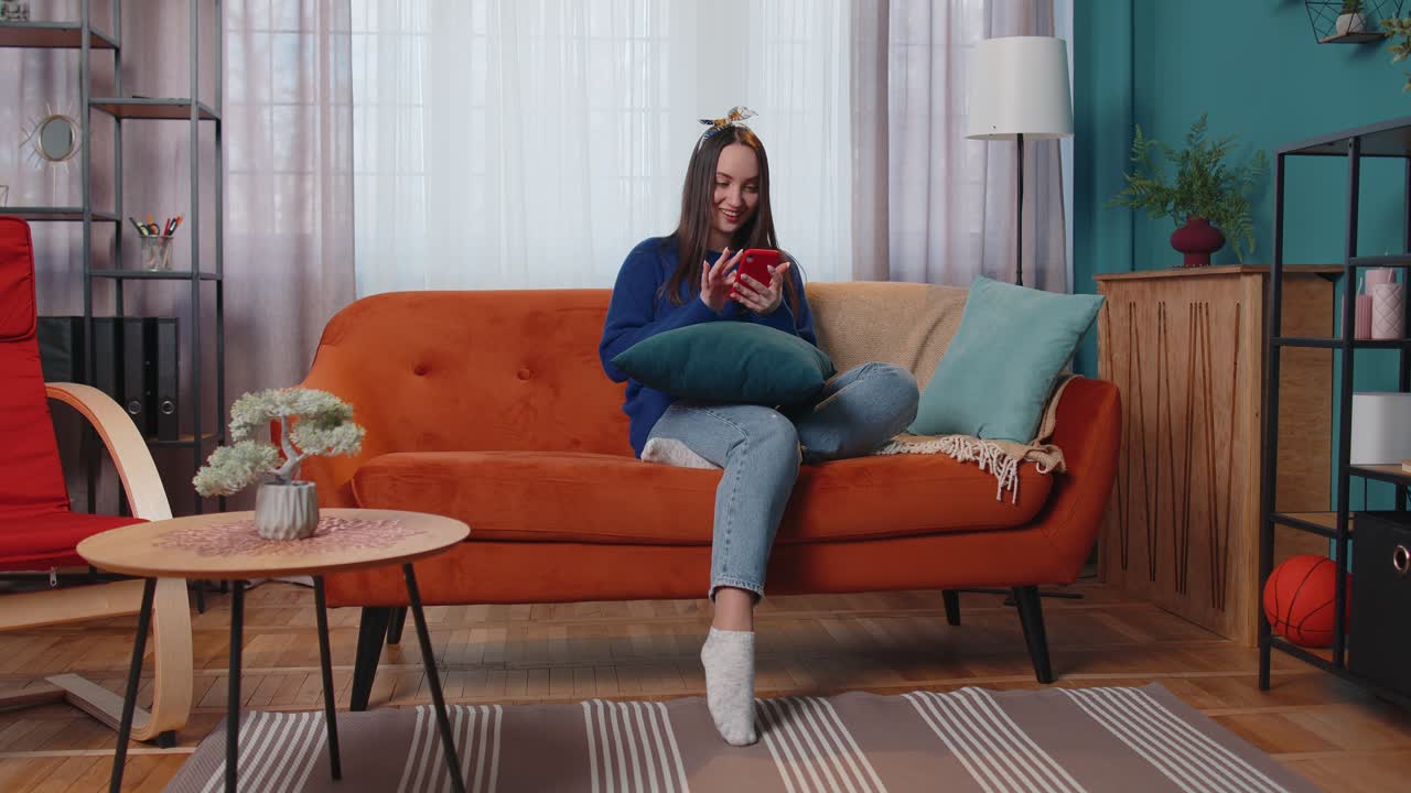 성인 젊은 여성은 집에서 휴대 전화를 사용하고, 타이핑하고, 브라우징하고, 와우, 네, 훌륭한 큰 승리를 발견했습니다.