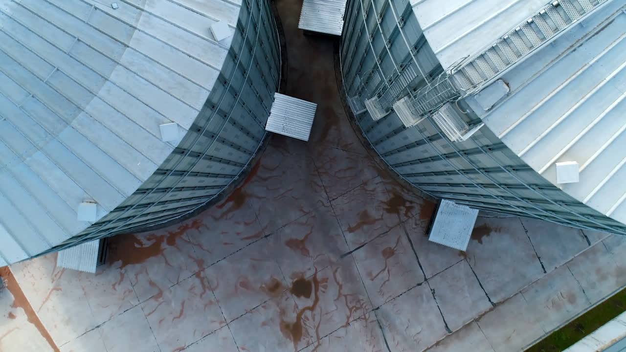 Modern agricultural containers. Metal grain elevators. Large storage tanks for storing grain. Metallic bins. Aerial view. Motion camera top down.