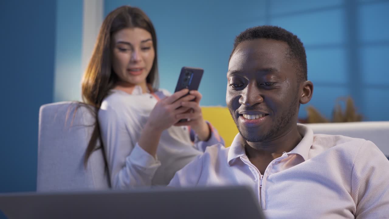 un joven africano feliz y su esposa blanca divirtiéndose en casa, charlando, ocupados trabajando como pareja multiétnica.