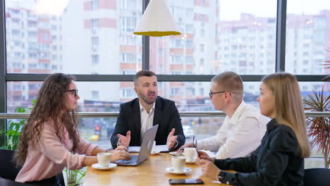 Little business talk at the cup of coffee. Business colleagues gathered together to listen to their boss. Window with cityscape at backdrop.