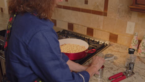 woman pours canned ingredients in to sauce pan with chick pea dish in slow motion