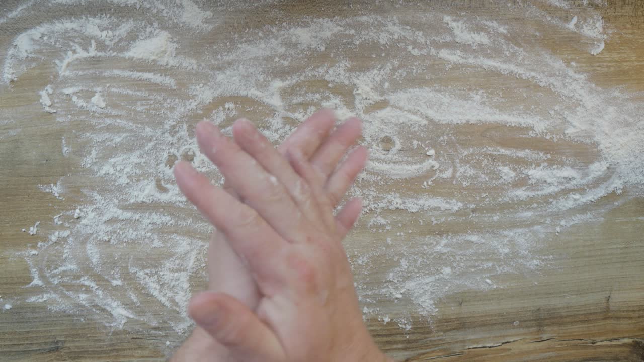 A baker, preparing to bake buns, sprinkles flour on the pastry board