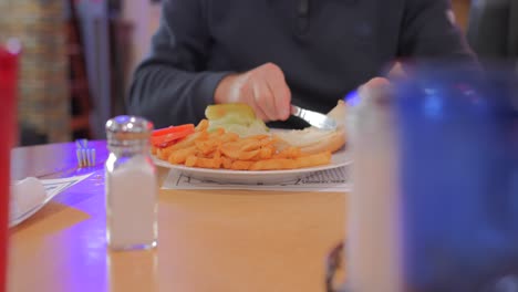 persona esparciendo mayonesa sobre pan en un plato con papas fritas en el restaurante de hamburguesas