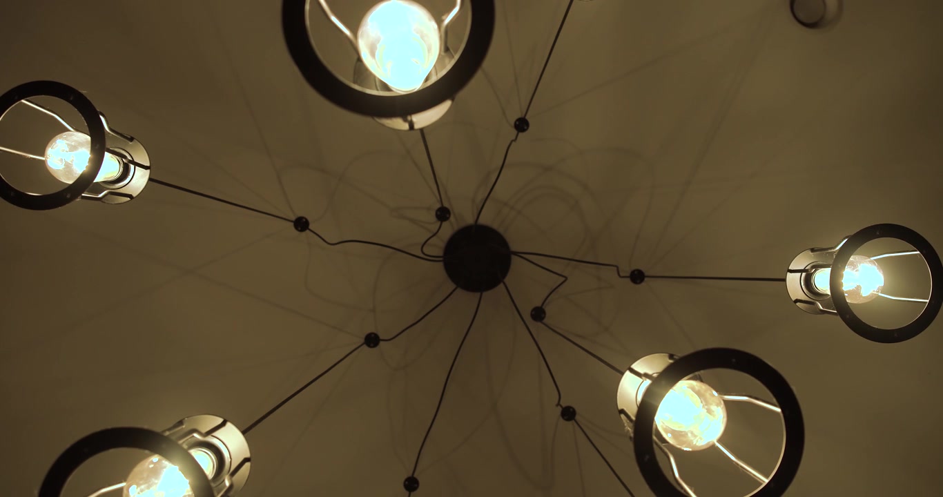 Looking up at a modern ceiling light fixture with glowing exposed bulbs. Symmetrical indoor lighting design creating a warm contemporary atmosphere and decorative architectural detail.