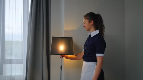 a maid in a hotel room turns on a lamp