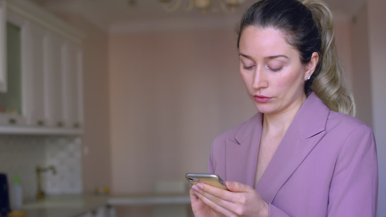 A woman attentively uses her smartphone in a stylish, bright kitchen. She seems to be organizing her day or checking important messages during her morning routine