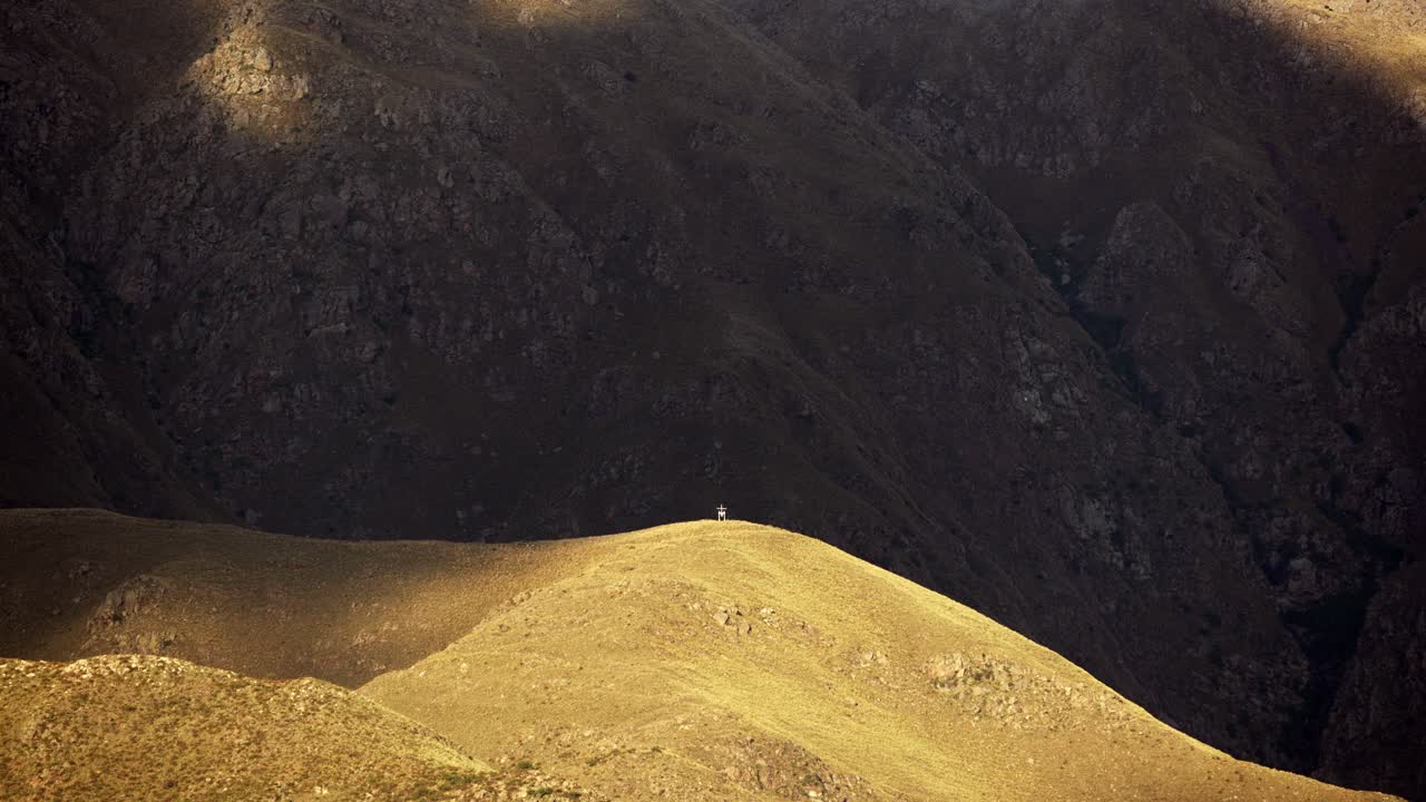 Time-lapse of cloud shadows over the mountains at sunset. Visible landmark at the top of a hill.