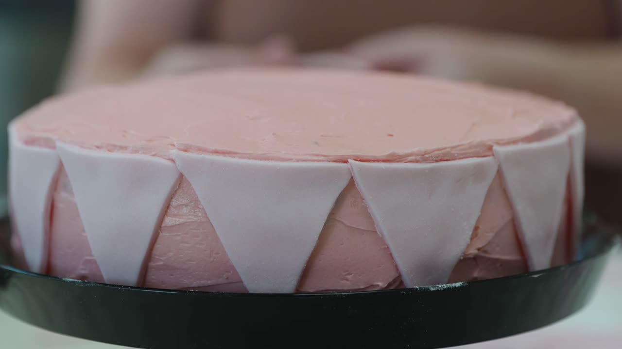 A person places pink fondant triangles to make bunting flags on a pink frosted buttercream cake