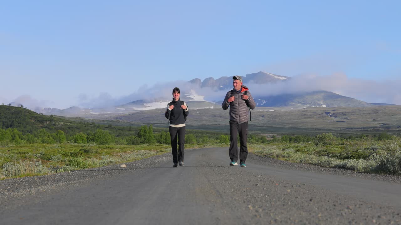 pareja de senderismo con mochilas en una carretera con montañas en el fondo. dovrefjell sunndalsfjella parque nacional es un parque nacional en noruega. hermosa naturaleza paisaje natural de noruega.