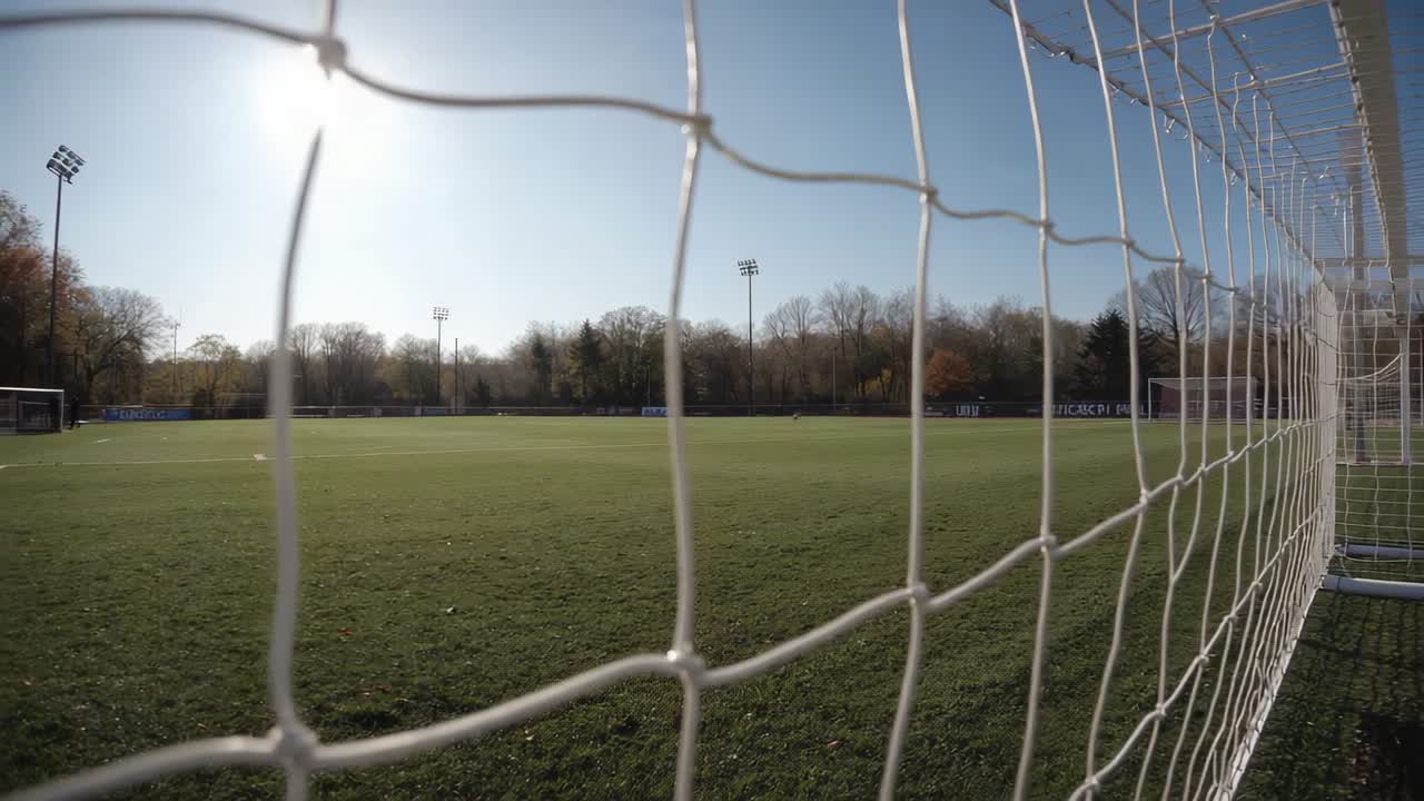 Soccer goal net rippling from light breeze, camera motion nudging frame, sun casting long shadows