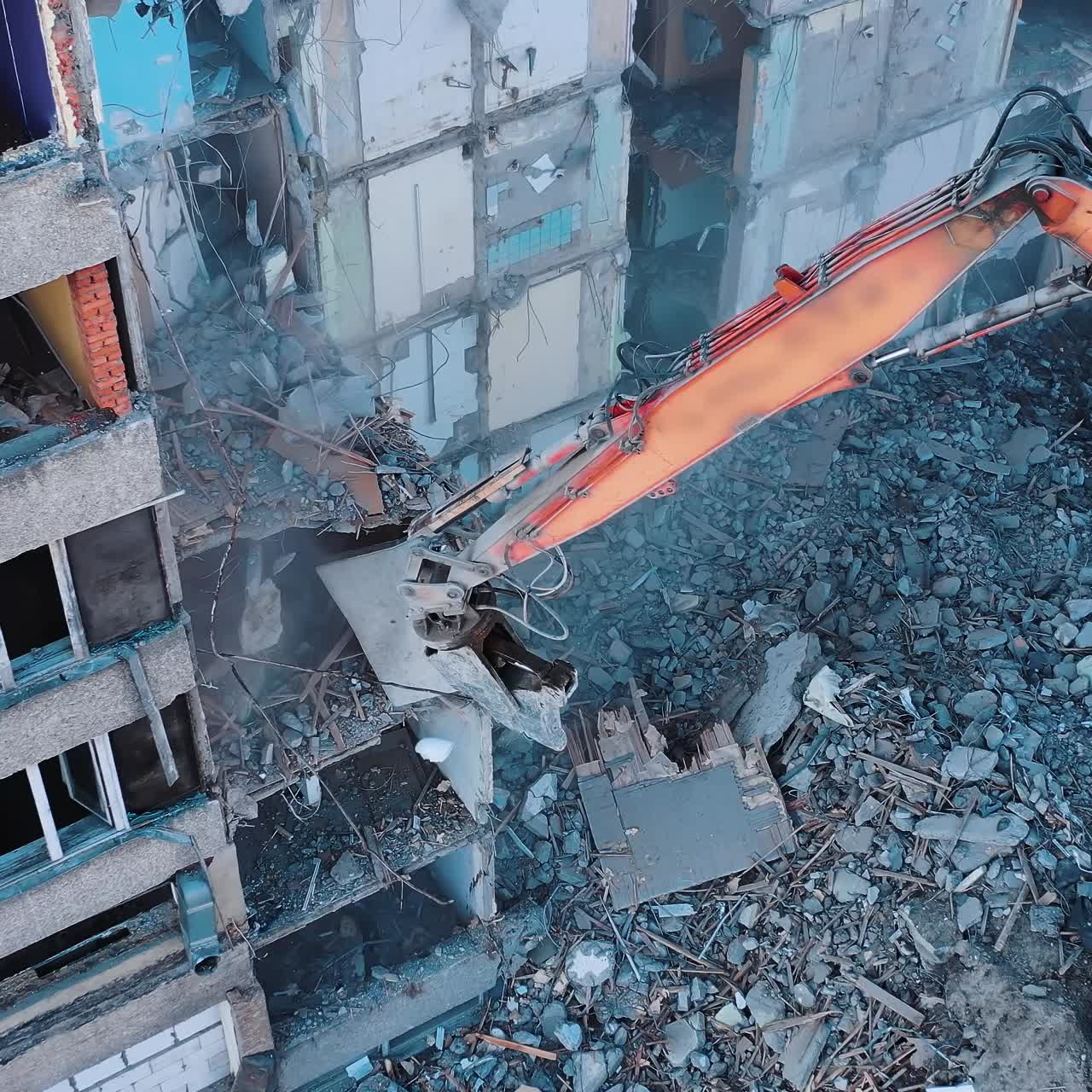 Excavator crashing floors of an old building and dusty debris falling down. Disassembling of collapsed structures. View from above