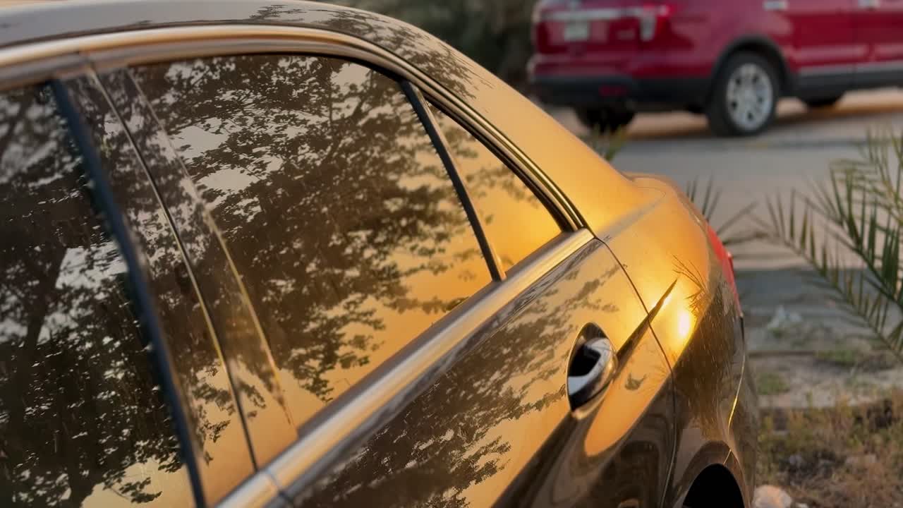 Una berlina scura parcheggiata in un parcheggio durante l'ora d'oro. La vibrante luce del tramonto si riflette sul finestrino e sulla carrozzeria lucida, creando un'atmosfera calda, cinematografica e di lifestyle.