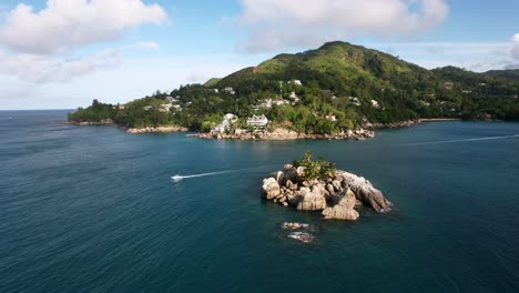 Mahe-Seychelles-cinematic-shot-of-small-island,-passing-boat-and-the-main-land-of-Mahe