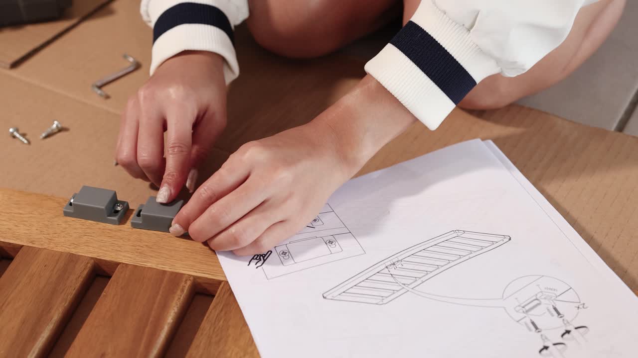 Hands assembling furniture with magnets on a wooden surface using illustrated instructions. Bright lighting, close-up view, 13-second duration