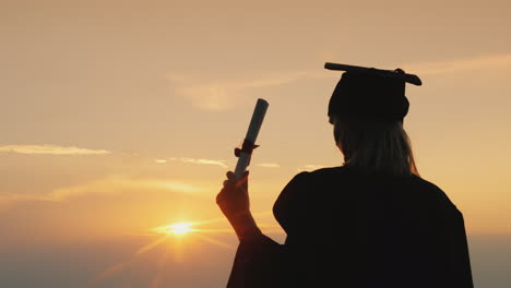 graduate with a diploma looks at the sunrise over the sea - perspective and inspiration concept