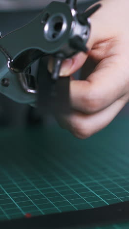 cu: experienced worker makes holes in black leather cloth with punch pliers on green cutting mat closeup