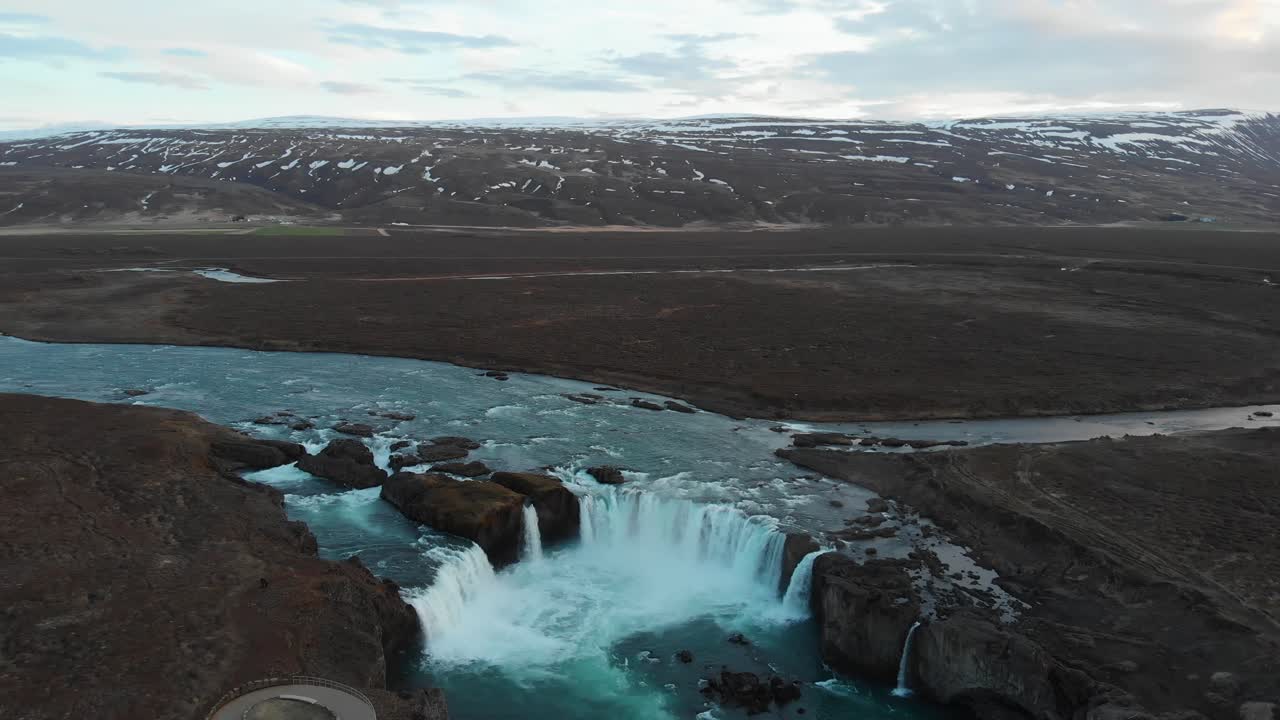 The extremely popular waterfall Godafoss filmed from an aerial view showing the amazing surroundings of snowcovered mountains in the background and the river flowing in the rocky landscape