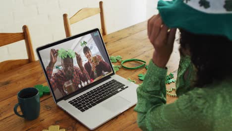 Smiling-diverse-couple-with-beer-wearing-clover-shape-items-on-video-call-on-laptop