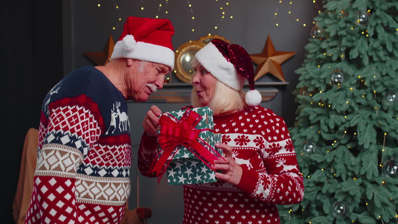 el abuelo regala una caja de regalos de navidad a la abuela sorprendida, una feliz pareja de mayores con sombreros.
