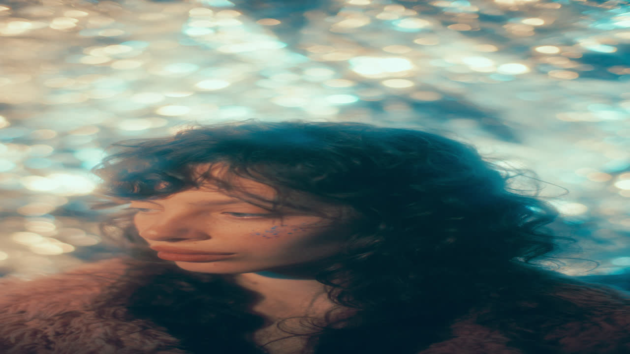 Young Pensive Woman with Glitter Cheeks against Glowing Bokeh Lights