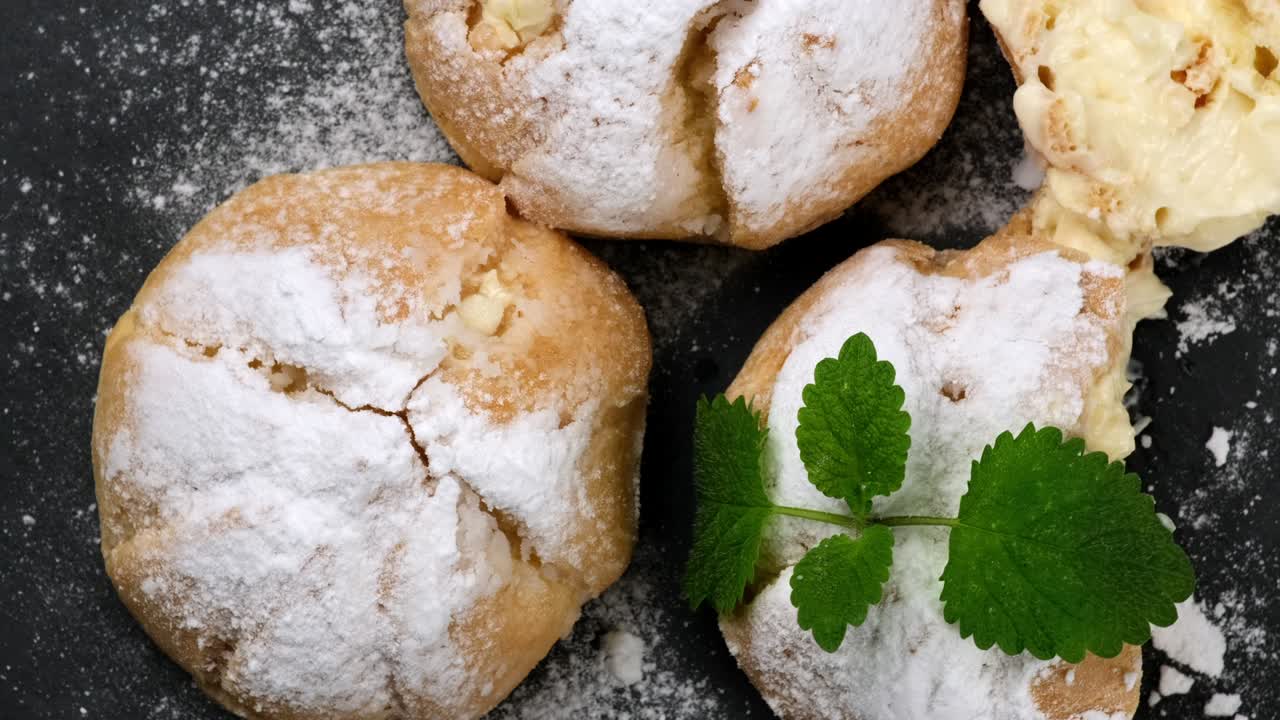 eclairs de crema al horno y salpicados de azúcar en polvo y decorados con una hoja de menta en una tabla negra