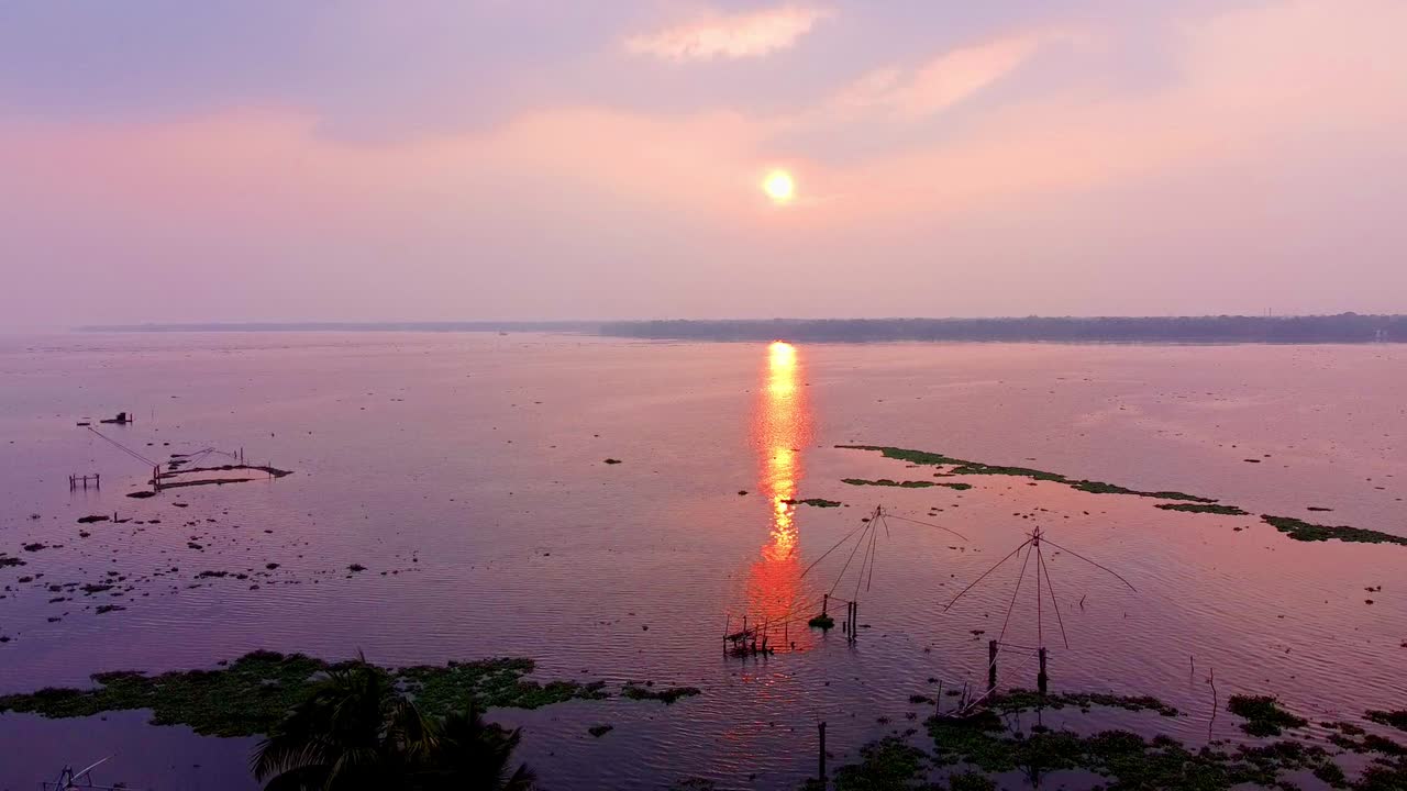 Chinese fishing nets silhouetted against a dramatic purple and pink sunrise , sunset over Kerala backwaters. Aerial view of reflection and tranquil water