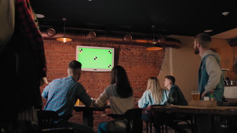 a group of friends in the pub looking at the green tv screen jump out of their seats and rejoice