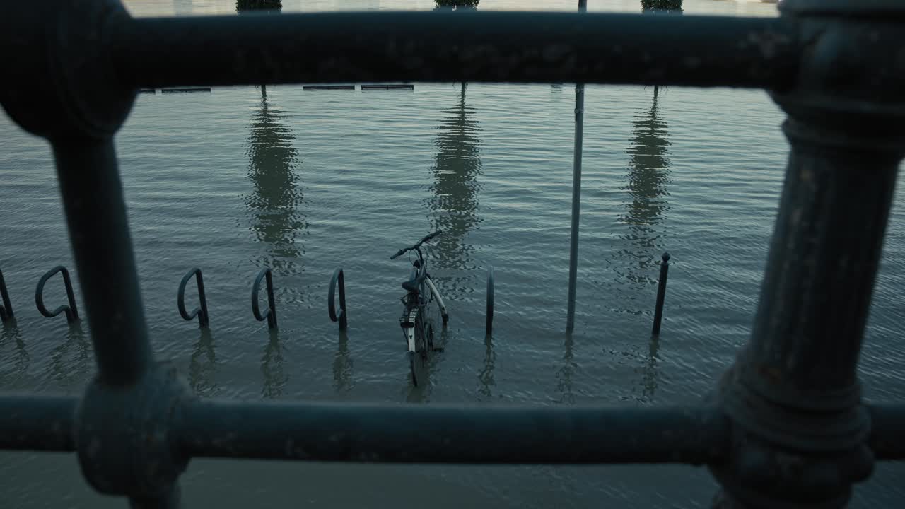 Submerged bicycle locked to a flooded bike rack with water reflections, seen through a railing, Budapest, Hungary