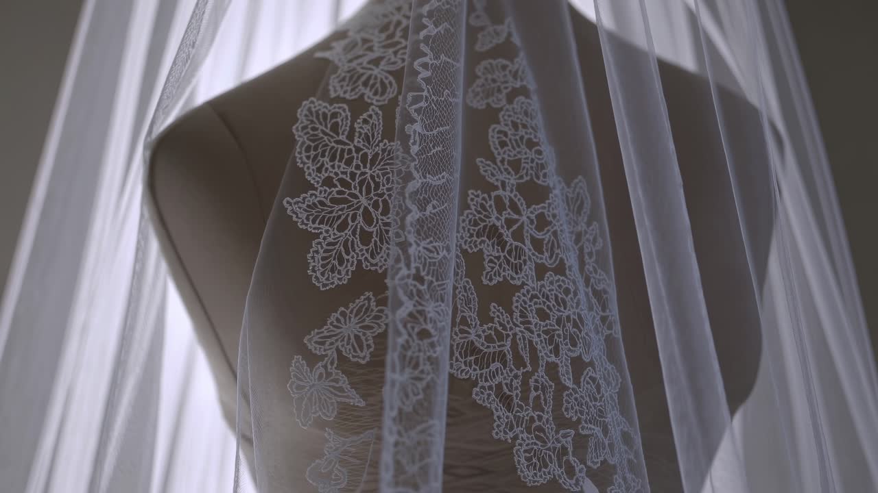 Ripresa video ravvicinata di un velo da sposa in pizzo drappeggiato su un manichino, che mostra intricati motivi floreali