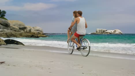 vista lateral de una pareja caucásica montando una bicicleta en la playa 4k