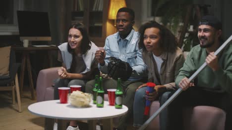 four friends sitting on the couch looking at a screen and celebrating