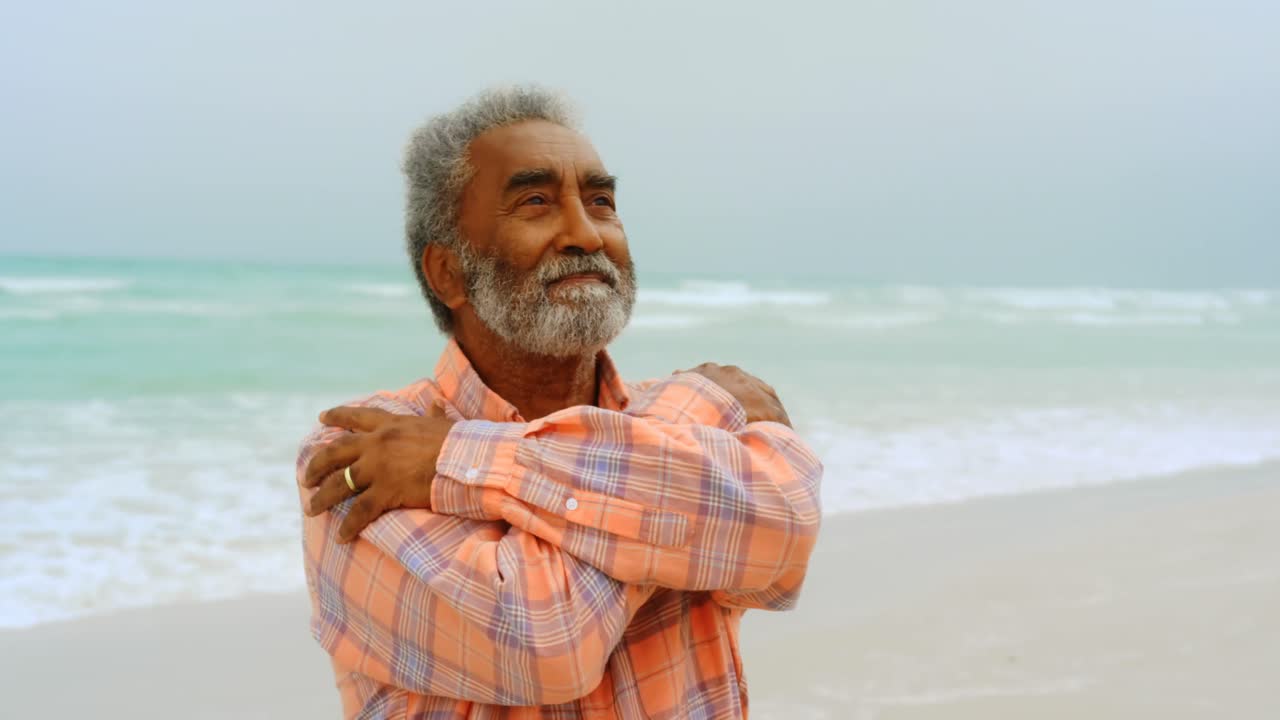 Front view of thoughtful active senior African American man shivering on the beach 4k