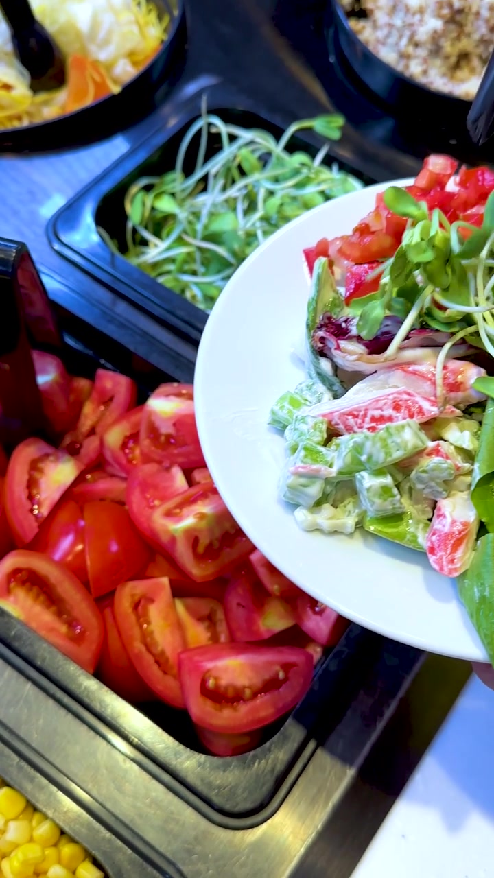 Un cliente riempie il piatto con verdure fresche a un luminoso buffet di insalate; movimento ravvicinato a mano libera.