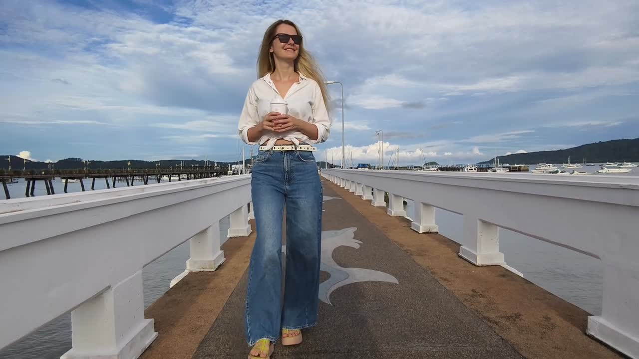 mujer caminando por un muelle con una bebida