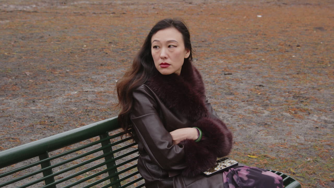 An emotional Asian woman waits on a park bench and sighs in annoyance