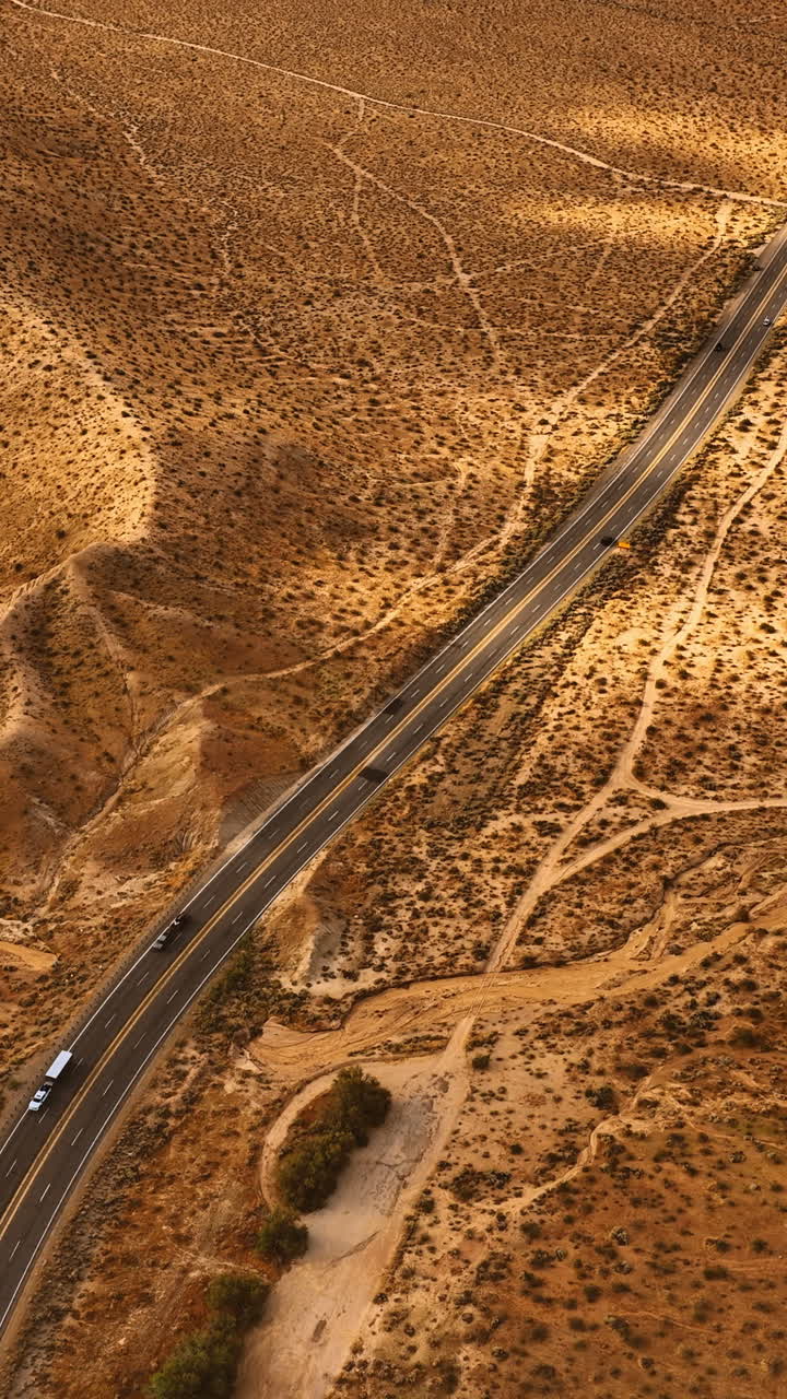 View of the highway with moving cars along the dry desert. Aerial perspective on the bare deserted landscape of Nevada. Vertical video