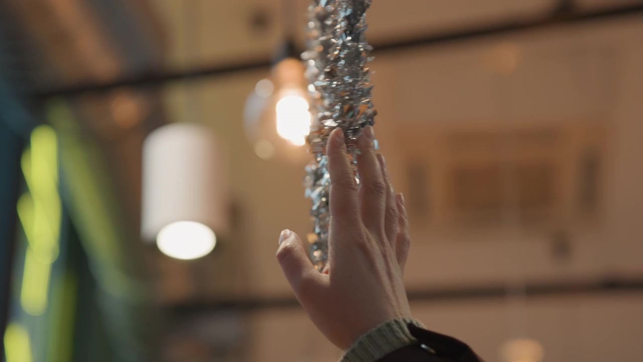 Luci brillanti del negozio decorano l'atmosfera natalizia. Mani che assistono posizionano un ornamento scintillante in un vivace ambiente di vendita al dettaglio. Una mano che aiuta attacca una stella lucente all'illuminazione festiva del soffitto del negozio.