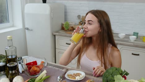 Girl-eating-raw-sprouts-buckwheat-with-nuts,-drinking-orange-juice-in-kitchen.-Weight-loss-and-diet