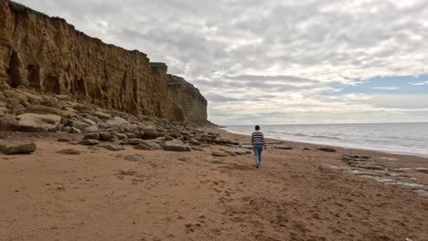 a women walking along a jurassic coast beach in dorset. the camera moves sideways to the right as the female walks away along the beach wide the sea on the right and the cliffs left.