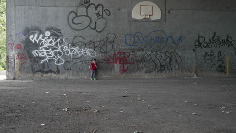 slow motion video of a young little boy in a red t-shirt leaning on a graffiti wall and running towards camera