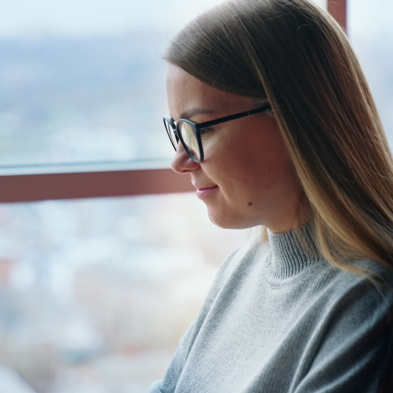 Happy positive lady puts on glasses and starts her work on laptop. Employee in a comfortable new office with panoramic window