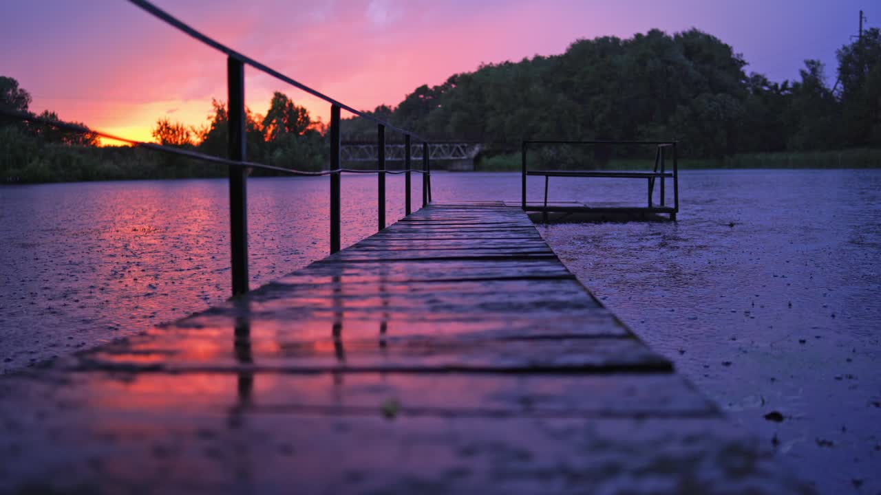 Amazing view of rain falling on the water and footbridge at sunset. Wet wooden bridge over the lake with nobody in the evening in rural place.