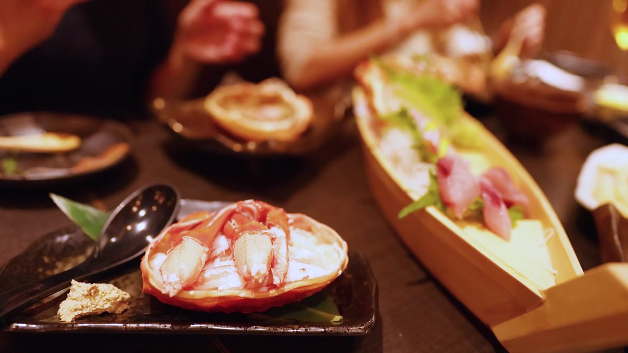 Primo piano di commensali che usano le bacchette per mangiare zampe di granchio fresche e sashimi in un ristorante.
