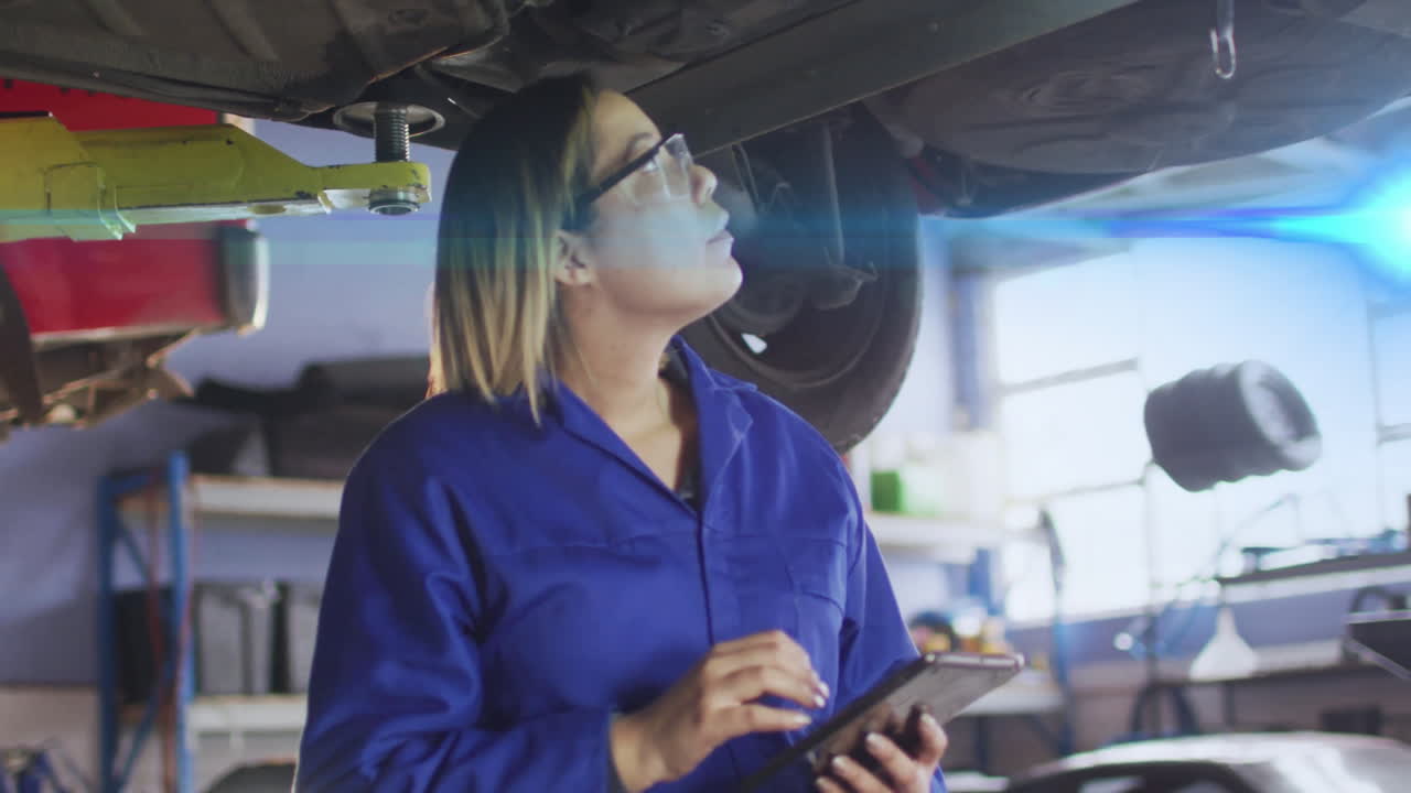 Female mechanic using tablet in automotive repair shop under lift arm, with animated data icons