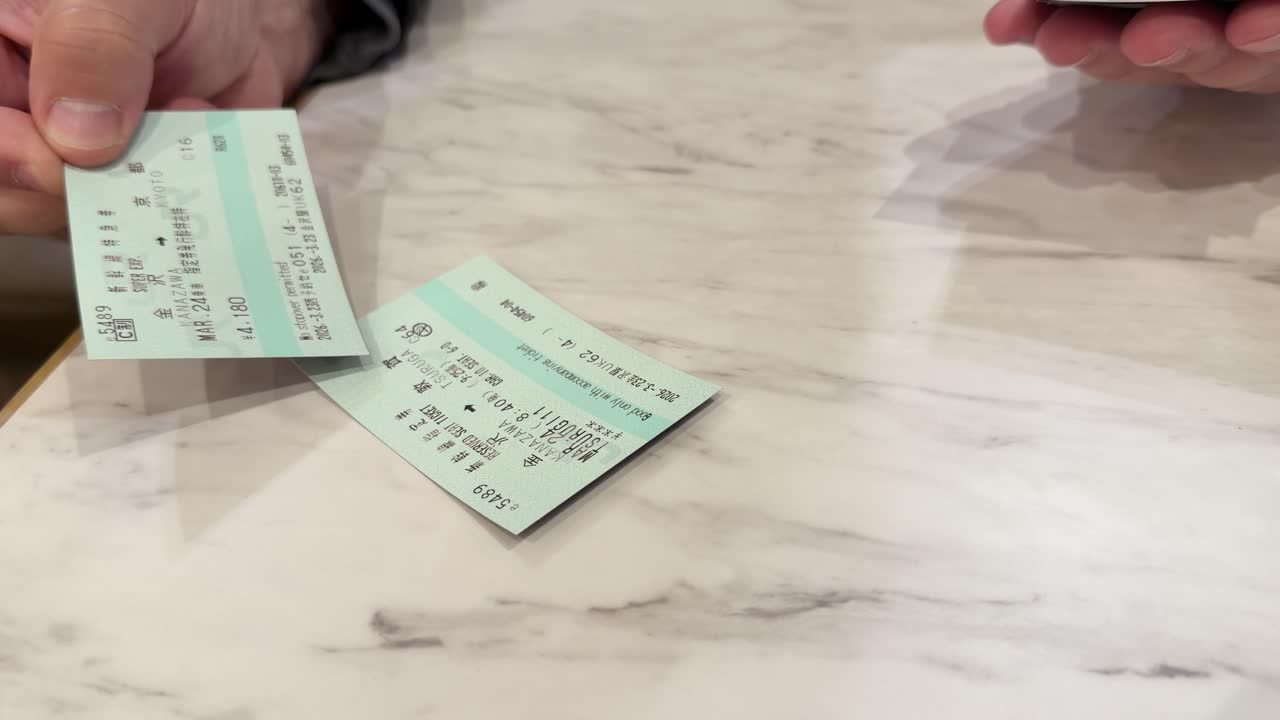 A person holds green Japanese train tickets over a marble table in a static shot