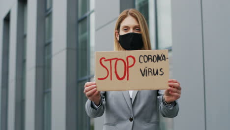 portrait of caucasian elegant young woman in facial mask showing stop coronavirus" signboard in the street"