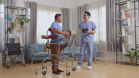 full body side view of asian male nurse with a tablet talking to a patient standing in walker, laughing, and punching each other's fists during a physical therapy at home